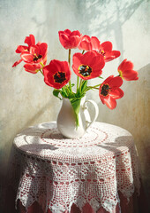 Rustic still life with flowers on a table covered with a white crocheted tablecloth. White jug with...
