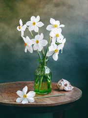 Still life of vase with daffodils flowers on a wooden table. Daffodils in a green glass vase on a round table.