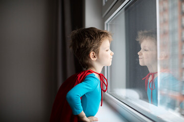 Boy dressed as a super hero in a red cape plays alone at home