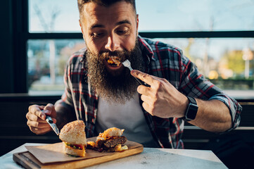 Bearded man sitting in a restaurant and eating a fresh tasty burger
