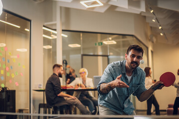 Young people playing table tennis in the office at work