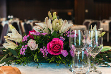Detalle de una mesa de boda decorada con un ramo de flores. Varios tipos de copas de vino sobre la mesa.