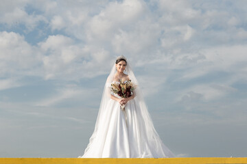 Fototapeta na wymiar Uma jovem mulher usando um vestido de noiva com céu nublado ao fundo.
