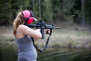 Woman shooting a rifle and the ejected cartridge case in the air.