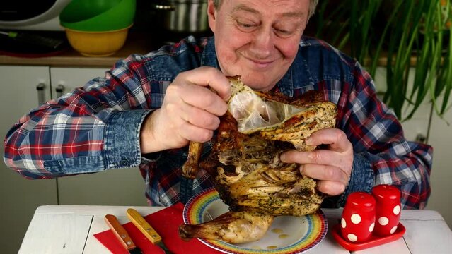 Senior adult man with appetite eating toasted fried chicken at table in home kitchen.