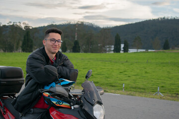 hombre con lentes, sentado en una moto y fondo de naturaleza 