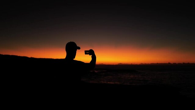 Silhouette of man taking photos on the phone at sunrise