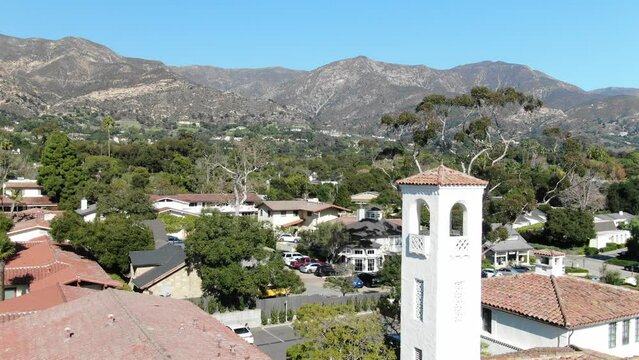 Downtown Montecito aerial close up of clock tower with homes and mountains in background on blue sky day in spring