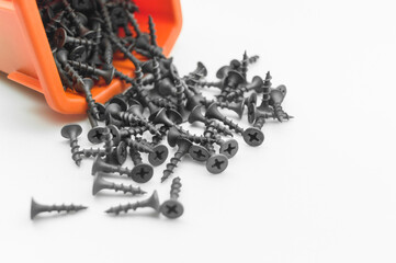 Black screws in orange box. Placer of metal fasteners. Close-up of short screws. Selective focus,...