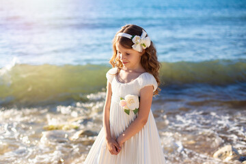Fototapeta na wymiar Beautiful little girl with curly brunette hair walking near the sea and dreaming 