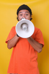 Asian casual guy isolated on yellow background using megaphone with surprised expression. 