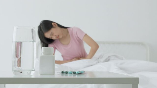 Young asian woman sitting on bed pain stomach or bowel with disease constipation or indigestion in bedroom at home, unhappy female sick and menstruation and stomachache, medical and health concept.
