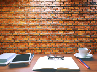 On the brown table, there are notebooks, books, pens, diaries, white coffee mugs. The front is a red orange brick wall.
With copy space.