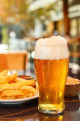 Transparent yellow beer with high foam in a glass and french fries on a table in a street cafe