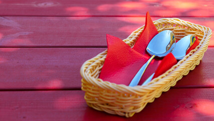 Two metal spoons lie on red paper napkins in a cutlery basket on a red wooden table. The idea of...