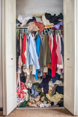 messy closet overfilled with colorful woman clothes on hangers and stuffed in any available space, need for declutter concept