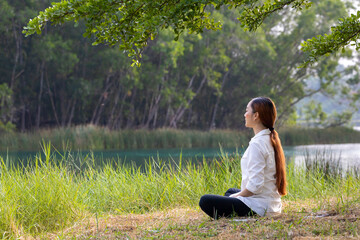 Woman relaxingly sitting and practicing meditation in the public park to attain happiness from...