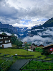 Fototapeta na wymiar Lauterbrunnen, Switzerland - August 19, 2019: Beautiful view of the Alpine Lauterbrunnen valley with wooden chalets in the Jungfrau region. White clouds cover the mountains. Vertical