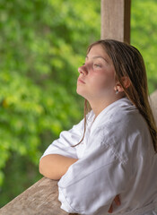 Little Caucasian Girl relaxing on a wooden balcony wearing a white bathrobe with opened eyes