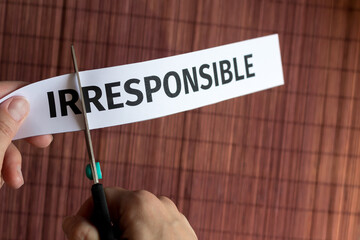 human hand cuts with scissors a piece of paper with the inscription irresponsible