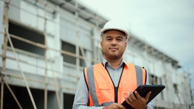 Confident asian engineer man with tablet for checking and maintenance to inspection at modern home building construction. Architect looking camera with white safety helmet in construction site