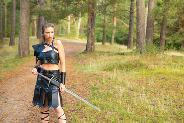 swordswoman wearing leather armor with sword patrols the wooden road - obrazy, fototapety, plakaty