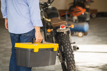 Fototapeta premium Technician man carrying toolbox, Mechanic repairing motorcycle in repair shop, Man repair motorbike in garage, Mechanic fixing motorcycle