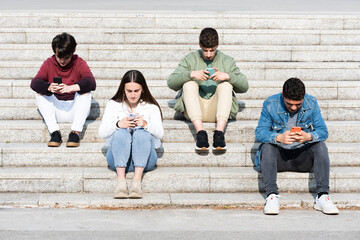 Teenager friends sitting on stairs and using their phones. Digital addiction and social distancing...