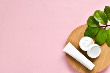 Natural cosmetics, skincare product - cream, lotion and micellar water on wood board on a pink background with green leaves plant. Flat lay with copy space.