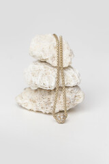 Jewelry fashion photography. Gold necklace with pendant displayed on decorative stones, studio product shot.
