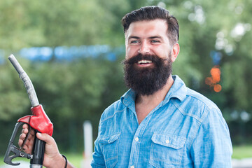 Man on petrol pump filling nozzles. Gas station. Portrait of bearded man hold fueling nozzle...