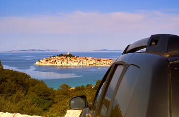 Impressions of a road trip through Croatia with a view over an off-road vehicle to a small island densely built with traditional houses in the Adriatic Sea