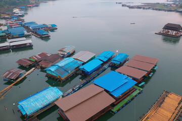 Fototapeta na wymiar Aerial top view of residential local floating houses in Mon village, nature trees with lake or river, Kanchanaburi, Thailand in urban city town in Asia, buildings.