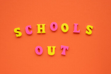 Light, vivid orange paper background. Yellow and pink wooden letters make School's out inscription. School's out concept. Top view, flat lay, copy space.
