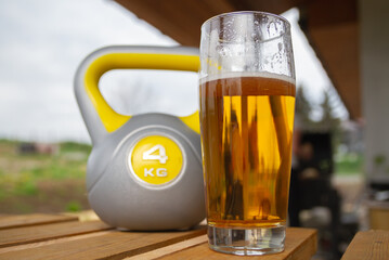 Glass of beer and heavy kettlebell weight in background. Contrasting alcohol with sports, choice...