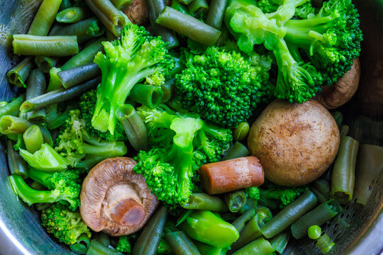 boiled green vegetables - broccoli, green beans and champignon mushrooms in stainless steel colander - full-frame closeup
