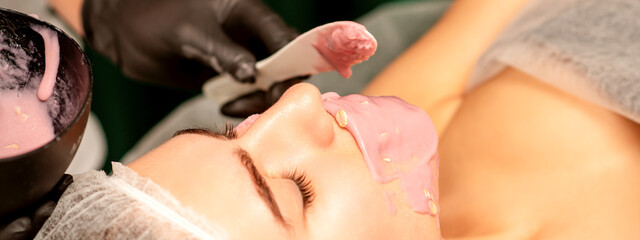 Obraz na płótnie Canvas Beautiful young caucasian woman receiving an alginic mask to the face in beauty salon. Facial skin treatment
