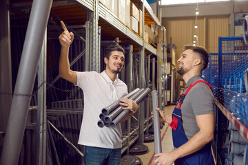Man in building materials store consults with seller on account of plastic pipes for plumbing. Between shelves in DIY store, friendly salesman in overalls talks about product that buyer is pointing at