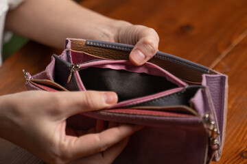 Woman opens empty wallet looking for money above table. Female hands hold violet purse on blurred background. Economical crisis concept closeup - obrazy, fototapety, plakaty
