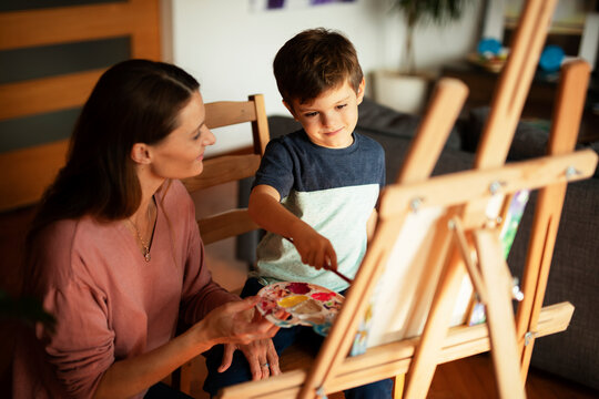 Mother and son painting at home. Little boy drawing with mom in living room..