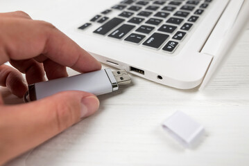Hand inserting a USB flash drive into a laptop on a white background. Close-up of woman's hand plug...