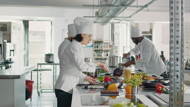 Female chef cooking gastronomy dish with vegetables on stove, making culinary recipe with bell pepper. Woman in uniform preparing food ingredients to cook delicious restaurant meal.