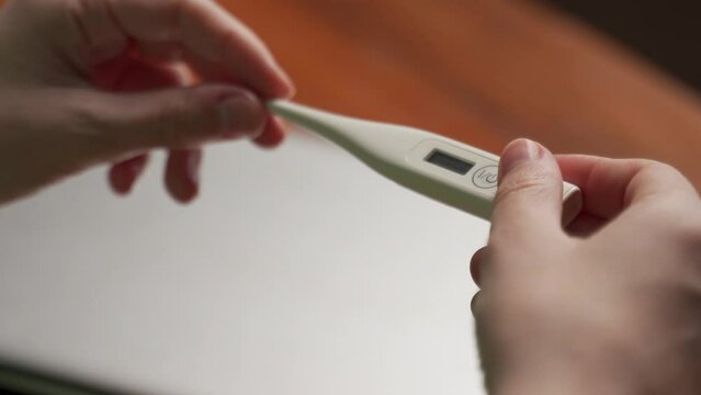 Female hands hold electronic thermometer with indicators on blurred background closeup. Woman checks temperature sitting near laptop at table in office
