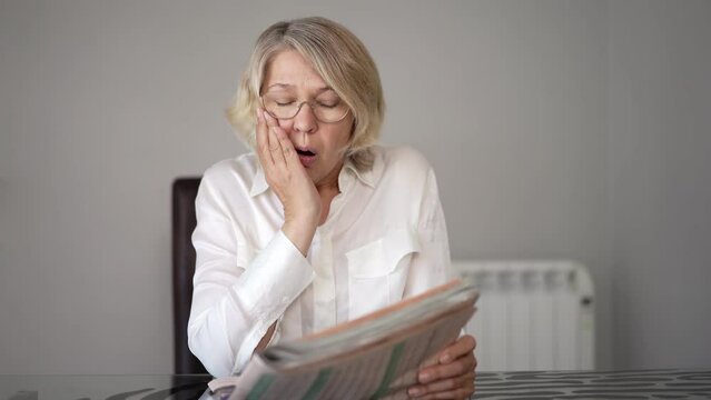 Senior woman reading newspaper at home. Bad news