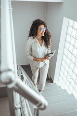 Shot of a young businesswoman using a digital tablet while walking up a staircase in an office. Businesswoman ascending office staircase. Professional Businesswoman Walking on Stairs