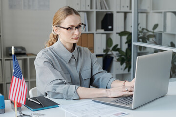 Horizontal medium shot of female visa service specialist sitting at desk working with application...