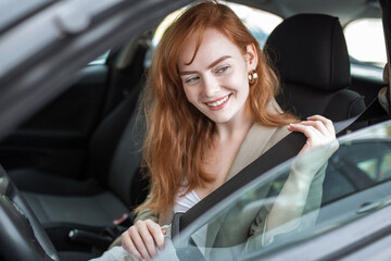 Fototapeta na wymiar Young woman sitting on car seat and fastening seat belt, car safety concept. Woman fastens a seat belt in the car. Caucasian woman driver fastening car seat belt while sitting behind the wheel car.