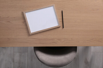 Chair near wooden table with blank frame and pencil indoors, top view. Mockup for design