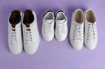 Set of new stylish white sneakers for entire family on violet background, flat lay