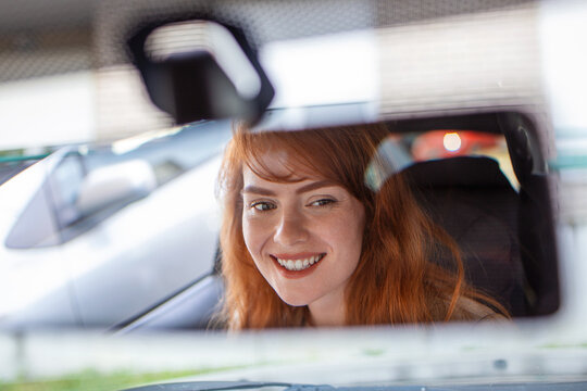 Woman view mirror of her car. Happy young woman driver looking adjusting rear view car mirror, making sure line is free visibility is good
